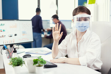 Pov of company employee waving while discussing with clients wearing face mask and shield during covid19. Manager speaking with remotely team during online conference while colleagues working in