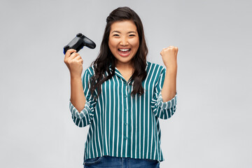 Fototapeta premium people, leisure and gaming concept - happy asian young woman playing video game with gamepad celebrating success over grey background