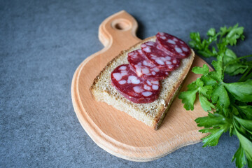 Sandwich on a cutting board, salami sausage and black bread