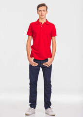 Obraz premium Photo of young confident man looking at camera. Full length Portrait of handsome guy with a calm emotions, posing at studio. Attractive male face. Teenager in a red shirt and blue jeans.