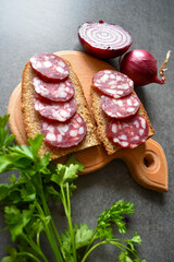 Snack sandwich black bread, salami sausage, fresh parsley, purple onion