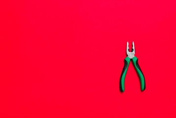 Quality green building pliers tool to compress something or repair a car or house on red background. Do it yourself instrument. Banner for advertising construction shop with copy space. Business card