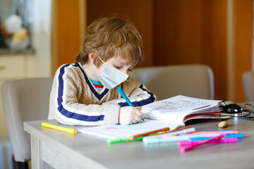 Hard-working school kid boy with medical mask learning during quarantine time from corona pandemic disease. Child on home schooling in coronavirus covid time, schools closed. Homeschooling concept