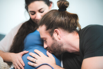 Husband kissing pregnant wife belly, concept of family love together, living at home