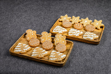Christmas ginger cookies in the shape of snowmen, fir trees and stars in the rectangular wooden plates on a gray background. The view from the top.