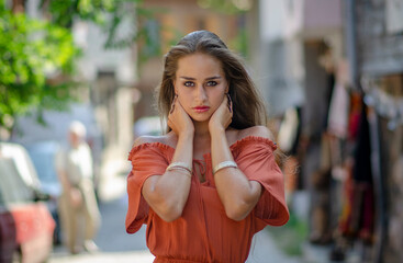 Beautiful young brunette woman with orange dress on a street urban background