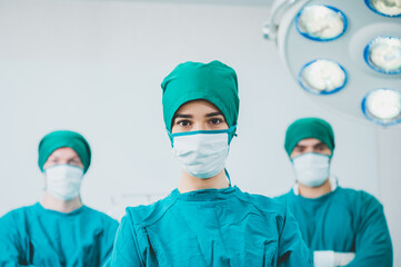 Fototapeta na wymiar surgical team in masks and uniform keeping arms crossed and looking at camera while standing in operating theatre together.