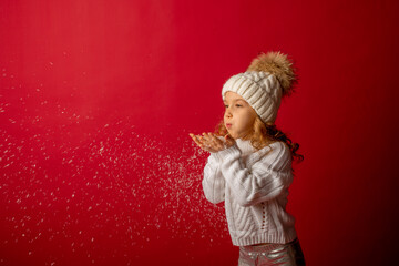 girl in  hat blowing on snow on red background