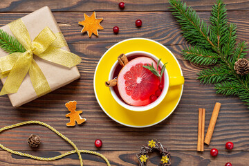 Yellow cup of tea with orange and spices near Christmas present and fir branch on wood