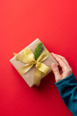 Female hand with a present decorated in minimalistic style on red background