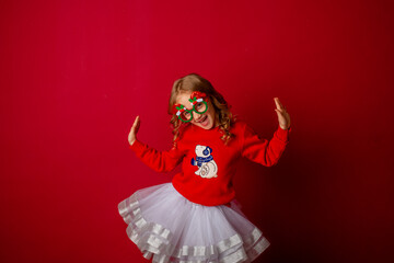 little girl in carnival glasses holds a gift on a red background, christmas