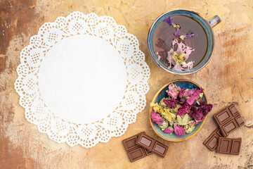 Obraz na płótnie Canvas A cup of hot herbal tea flowers chocolate bars and napkin on mixed color backgroundherbal tea