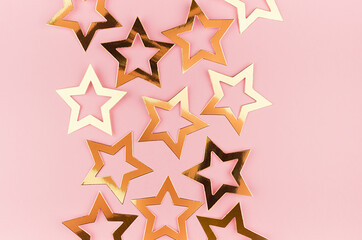 Bright gold glossy stars on soft light pink color, top view,  border.