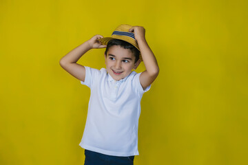 A little boy in a white shirt and straw hat on a yellow background.The boy takes off or puts on his hat.