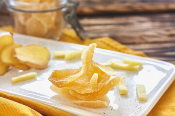 Candied ginger slices in a white plate on wooden table. Dehydrated oriental fruits. Healthy sweets....