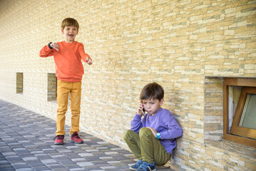 Portrait of little boy crying hiding his face with cruel kids pointing at him in background,...