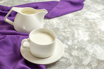 side close view of a cup of milk and a jug of milk on a purple napkin at the side on a marble backgound