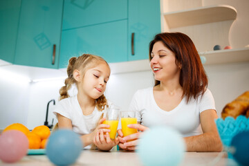 Mother with little girl drinking orange juice while they have breakfast together