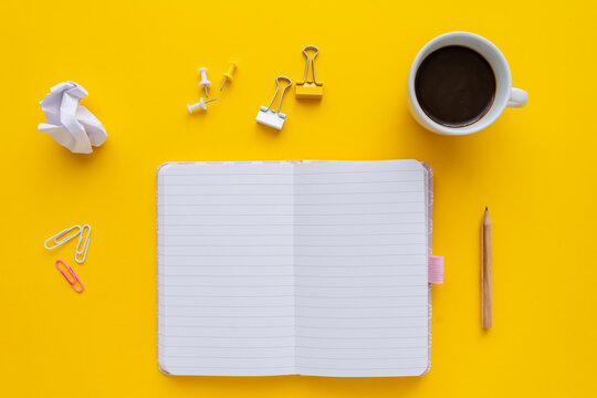 Ein leeres Notitzbuch mit einer Tasse Kaffee auf einem gelben Hintergrund. Flat lay, B&uuml;robedarf.