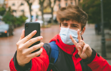 Guy with face mask and backpack taking a selfie in the street on a winter day.