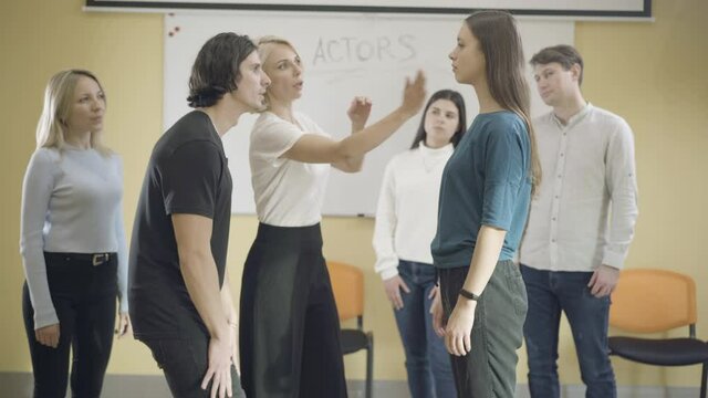 Group of male and female actors studying in auditorium. Professional Caucasian teacher showing slap in face to adult students. Professional acting and studying concept.