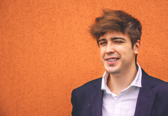 Guy in suit smiling on an orange wall.