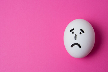 Fototapeta premium An egg with a sad face, on a pink background with copy space.