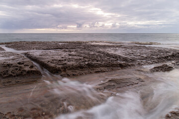A big rock in the coastline under cloudy sky.