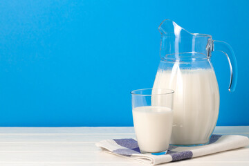 Glass and pitcher of milk against blue background