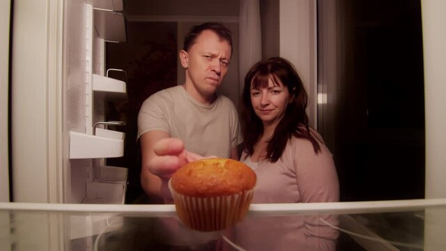 A married couple opens the refrigerator at night and finds there one spoiled cupcake