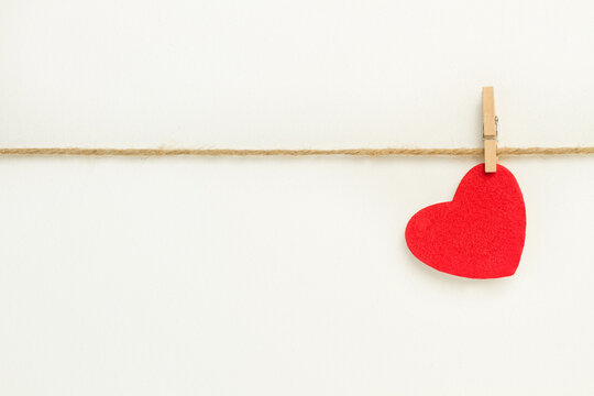 Un corazón de tela colgado con una pinza de un cordel sobre un fondo blanco liso y aislado. Vista de de frente. Copy space. Concepto Día de San Valentín, matrimonio, día de la madre, concepto de amor.