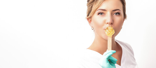 Obraz na płótnie Canvas Portrait of female cosmetologist holds a wooden stick with a wax covering her lips on white background