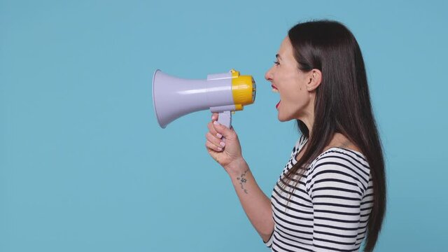 Side profile view of cheerful brunette young woman 20s in striped shirt posing isolated on blue background studio. People lifestyle concept. Looking aside screaming in megaphone turn around camera