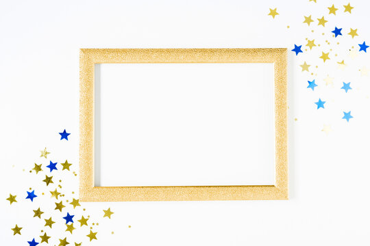 Festive background with gold and blue stars confetti. Shining golden stars, photo frame on white background. Flat lay, top view, copy space.