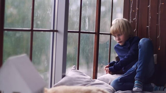 Sad boy sits by the window. Yearning child