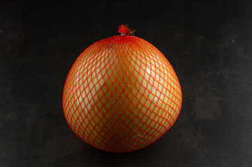 One pomelo fruit in a package on a black background.