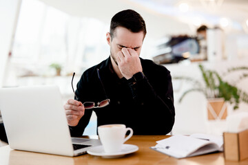 Give your eyes a rest Young tired freelancer man in black shirt suffers from pain and dryness in...