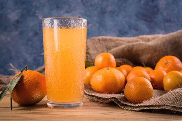 Fresh juicy tangerines or mandarins with green leaves on sack cloth and wooden table and glass of fresh juice.