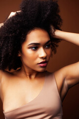 pretty young african american woman with curly hair posing cheerful gesturing on brown background, lifestyle people concept