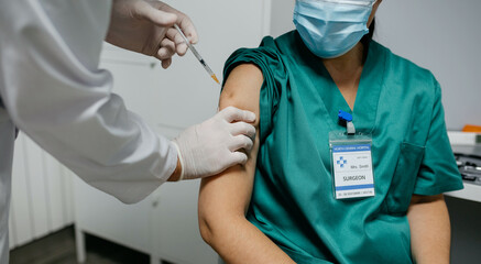 Unrecognizable female surgeon receiving coronavirus vaccine at doctor's office
