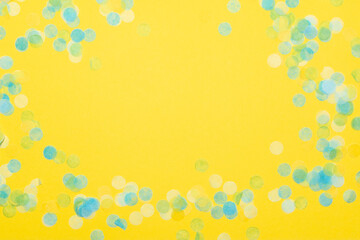 Blue green and yellow paper confetti on a vibrant yellow background