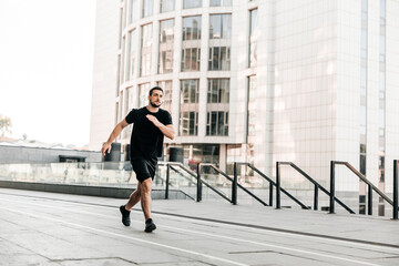 Young fit man doing urban running workout on asphalt road sprinting in sport and healthy lifestyle concept. Big city on background. Black sportswear. Caucasian man jogging.