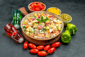 side close view of bowl of vegetable salad with vegetables and oil vinegar bottles on side on dark grey background