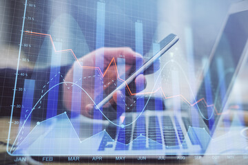 Double exposure of man's hands holding and using a phone and financial graph drawing. Analysis concept.
