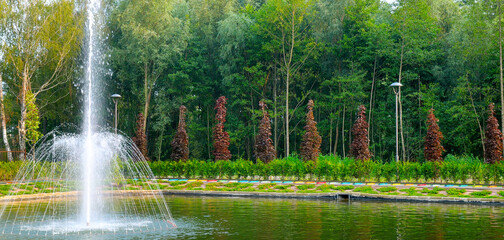 Fountain on a small lake in the city park of rest. Wide photo.