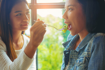 LGBT Lesbian Asian couple romantic moments eating vegetable salad in restaurant.