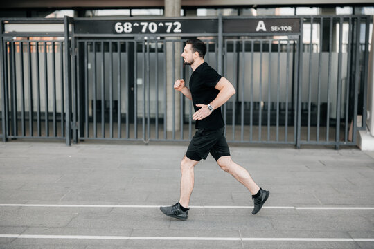 Concentrated male runner excercising at morning. Urban city lifestyle concept. Athletic man in black sport clothes and sneakers jogging outdoors. Healthy lifestyle. Man running. Active living.