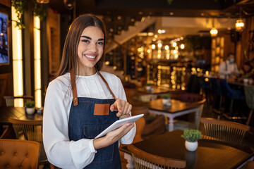Portrait of a happy waitress working at a restaurant using a tablet computer and smiling - food service concept. It pays to invest in quality tech for your store