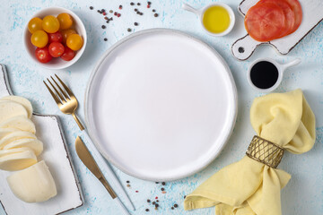 Empty white plate surrounded by cutlery and fresh vegetables