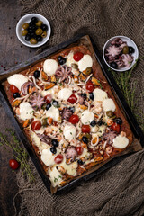 Rectangular homemade seafood pizza with octopus, shrimp, mussels and squid on a dark wooden background.